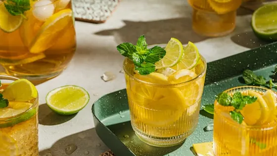 Iced lemon drink with mint on a green tray in warm sunlight, slices and limes around.