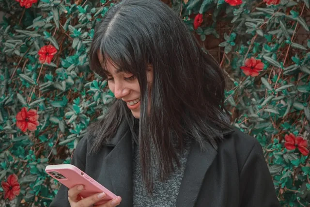 Smiling woman looking at her phone against a green wall with red flowers