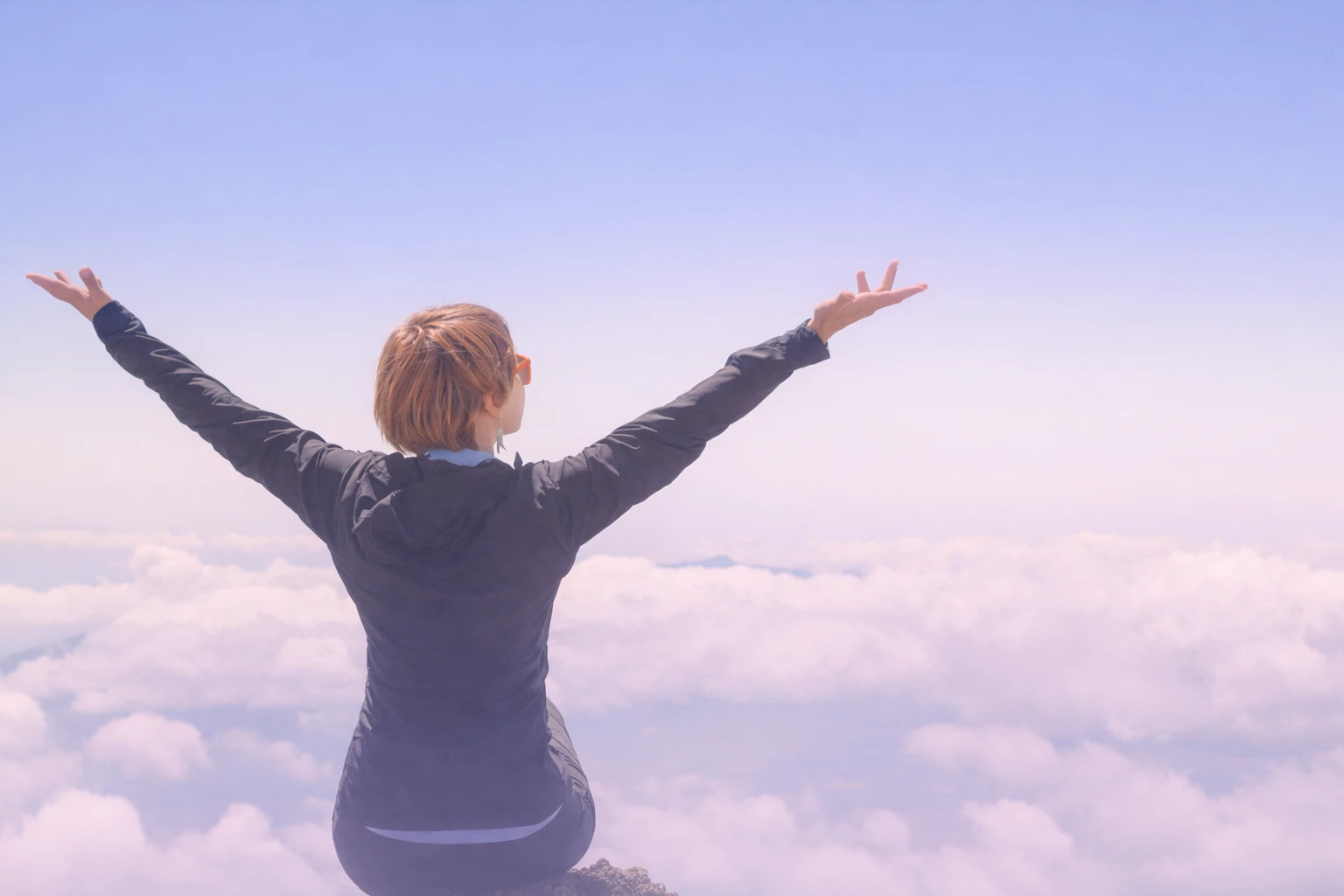 Person sitting above the clouds with arms open, symbolizing calm breathing and relaxation
