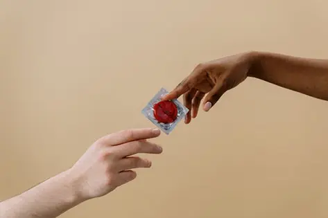 Two hands gently passing a condom, symbolizing trust and safety
