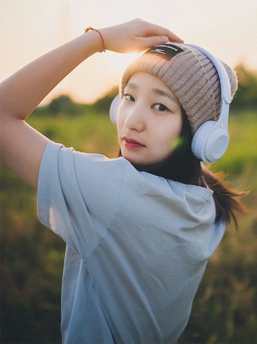 Woman wearing headphones in a field, turning toward the camera with a calm, relaxed expression