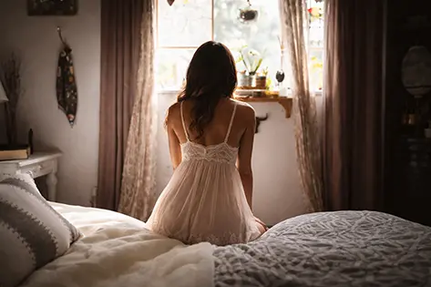 Woman sitting on a bed at sunrise in soft, calm morning light