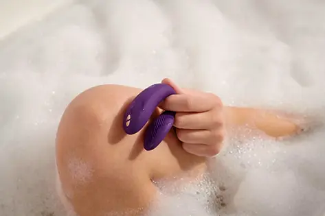 Soft intimate moment with a purple wearable vibrator held in hand during a relaxing bath