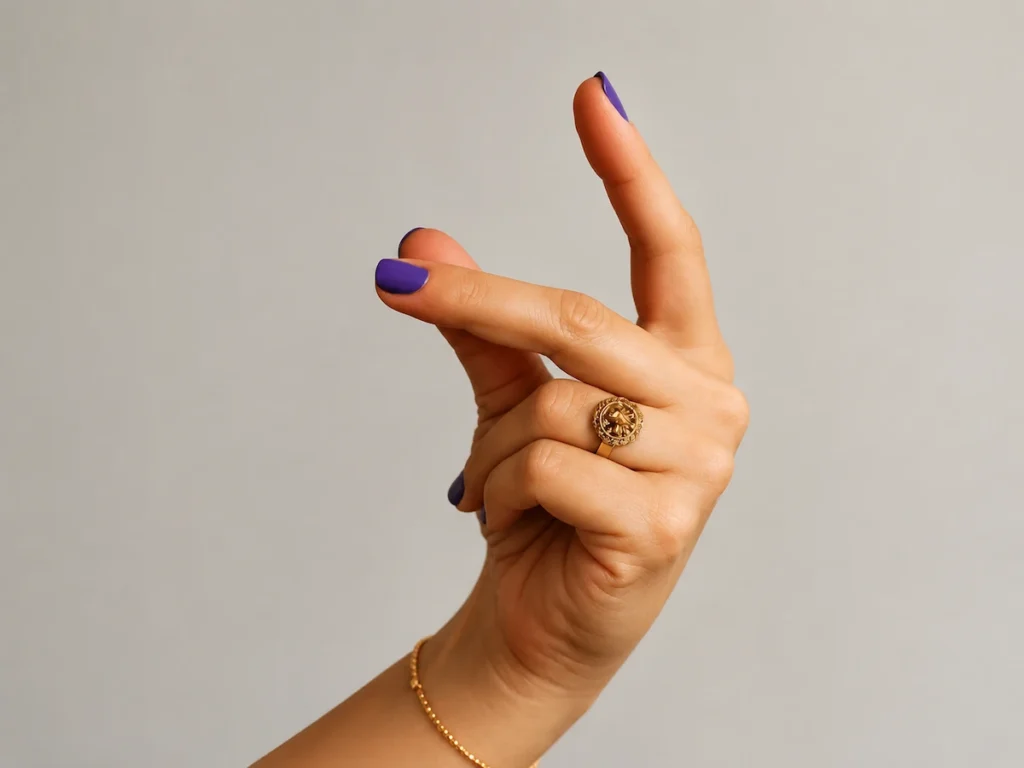 Close-up of a hand with purple nail polish and a gold ring making a playful snap gesture against a neutral background